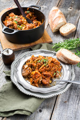Traditional Polish kraut stew bigos with sausage, meat and mushrooms as top view in a cast iron pot and pewter plate on an old rustic board
