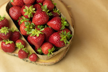 Fresh strawberries in a Kraft box on a wooden stand close-up. Open space, healthy food concept, plants, soil, organic natural products, natural food, vegetarian dishes, vegetables, raw, food festival