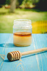 jar of honey and honey dipper on a blue wooden table in a garden