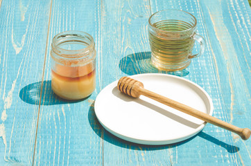 bank of honey with the dripping spoon in a plate and a glass cup of tea. On a blue wooden table
