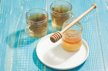 bank of honey with the dripping spoon in a plate and a glass cup of tea. On a blue wooden table