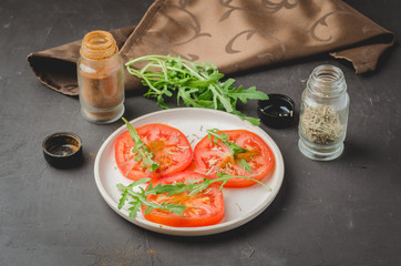 sliced tomatoes and arugula spices salad. Healthy food on a dark background.