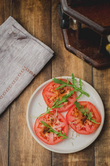sliced tomatoes and arugula spices salad. In a white bowl on a wooden background. Top view