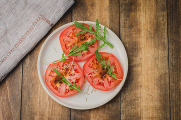 sliced tomatoes and arugula spices salad. In a white bowl on a wooden background. Top view