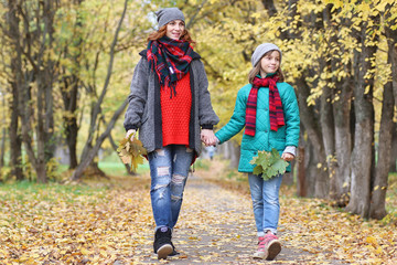 Young beautiful mother with her daughter on nature. A girl in a hat walks in the park. Girl in autumn city park in leaf fall.