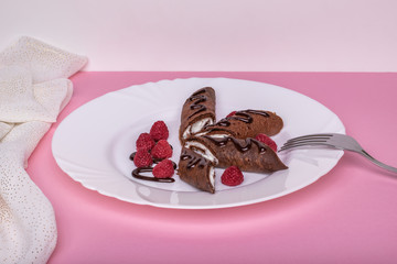 Chocolate pancakes stuffed with cottage cheese decorated with raspberries and chocolate. Pink background
