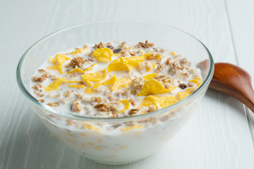 Glass bowl with cornflakes and milk, wooden spoon, closeup