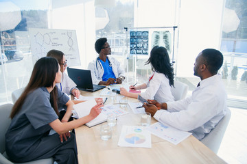 Multi-ethnic group of professional doctors discussing x-ray prints of patient in the meeting room...