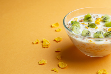 Glass bowl with cornflakes and milk on an orange background, side view