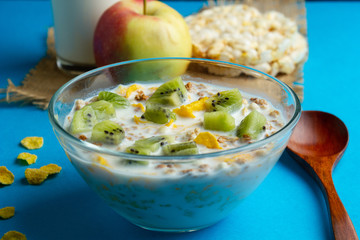 Glass bowl with cornflakes and milk on a blue background, apple, closeup