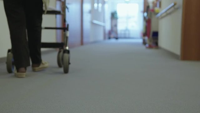 Old woman with rollator walking down a hallway