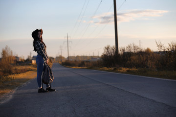 A young girl is traveling around the city hitchhiking. A beautiful young girl went on vacation. A female student in a cowboy hat on the road in autumn.