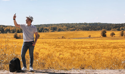 A young man is traveling in nature. Traveling with a backpack on the shoulders of a beautiful park. Hitchhiking with one bag in autumn.