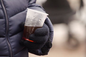 Gloved hand holding a plastic cup with tea. Street food in winter.