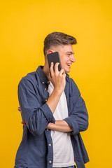 Handsome young man using his phone with smile while standing against yellow background.Young adult man talking on the phone scared in shock with a surprise face, afraid and excited with fear expressio
