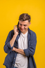 Handsome young man using his phone with smile while standing against yellow background.Young adult man talking on the phone scared in shock with a surprise face, afraid and excited with fear expressio