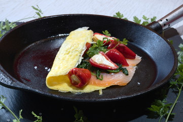 ketogenic food in a cast-iron frying pan with scrammbled quail eggs pepperoni cream cheese spinach and smoked salmon on a slate and white wood background