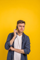 Handsome young man using his phone with smile while standing against yellow background.Young adult man talking on the phone scared in shock with a surprise face, afraid and excited with fear expressio