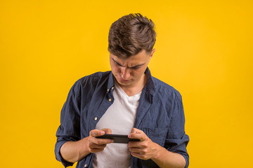 Attractive young man with smartphone on color yellow background. Portrait of an excited young man looking at mobile phone isolated over yellow background, celebrating