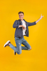 Full length portrait of an excited young man in white t-shirt jumping while celebrating success isolated over yellow background.