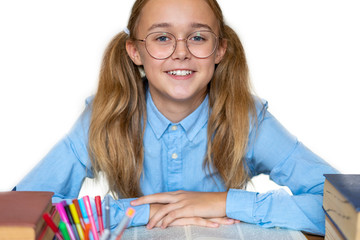 Joyful teen girl sitting at the table with pencils and books textbooks. Happy pupil doing homework at the table. Beautiful smiling teen girl with ponytails and expressive blue eyes with glasses