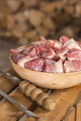 Chunks of raw meat in a clay bowl. Near skewers. Firewood in the background. Cooking kebabs. Vertical. Space for text