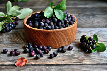 Black chokeberry in wooden utensils on old wooden boards.