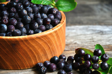 Black chokeberry in wooden utensils on old wooden boards.