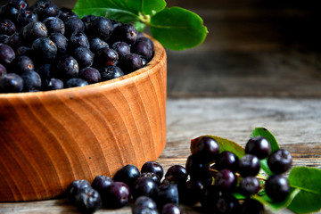 Black chokeberry in wooden utensils on old wooden boards.