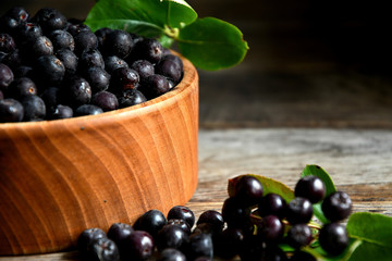 Black chokeberry in wooden utensils on old wooden boards.