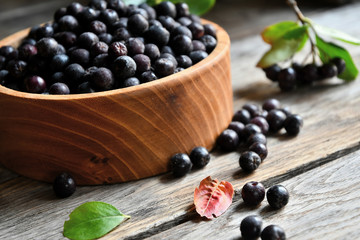 Black chokeberry in wooden utensils on old wooden boards.