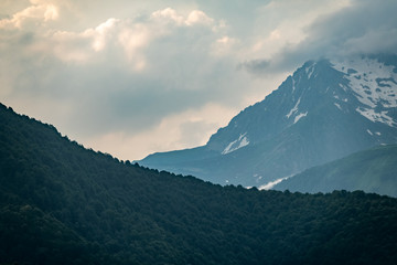 Mountain ranges with green and rocky slopes. Mountains with snowy peaks hidden in the clouds.