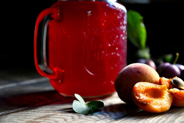 Compote of plums and apricots in a glass beaker with a straw on a wooden table.
