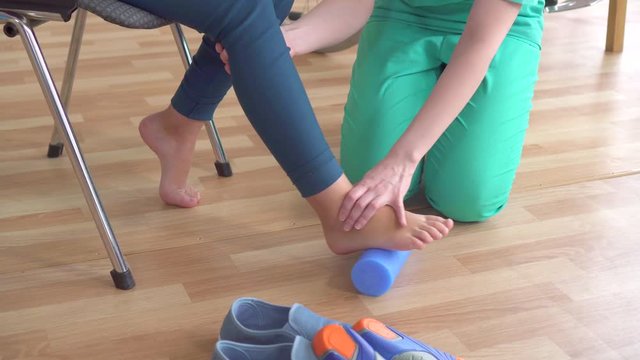 doctor helps a teenage girl in a wheelchair with orthopedic problems to do exercises to correct flat feet close up