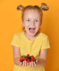 Young baby girl kid hold berries fruits in hands surprised happy laughing screaming on yellow 