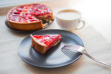 Still life with a Cup of coffee and sweet dessert with strawberries, cheesecake cake with slices of berries in jelly on top.