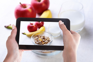 Female hands with a smartphone, on the screen of which is a photo of Healthy food with corn flakes cereal in a bowl, apple, banana and glass with milk. Morning breakfast.
