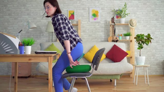 young woman sits on a round orthopedic pillow and starts working on a laptop