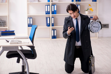 Young male employee in the office in time management concept