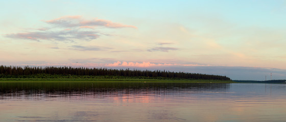 Bright orange sunset behind the clouds of sun on the banks of the Northern river Viluy under the blue sky in the spruce forest and silhouettes of boats and people in Yakutia.