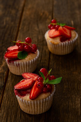 Fresh Strawberry fruits over homemade muffins decorated with mint leaves. Wooden table and black background.
