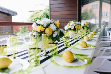 A celebration table served with green glassware decorated with whole lemons and bouquet of flowers
