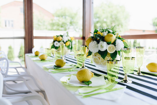 Summertime banquet table in veranda with stripy tablecloth decorated with whole lemons and bouquets of flowers and lemons