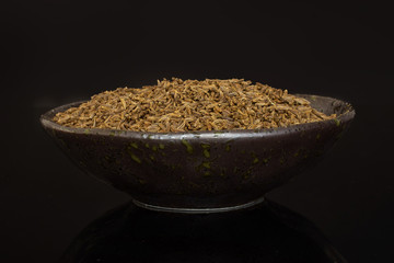 Lot of whole dry caraway fruits in a grey ceramic bowl isolated on black glass