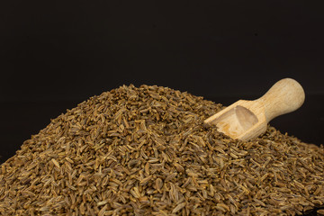 Lot of whole dry caraway fruits macro with wooden scoop isolated on black glass