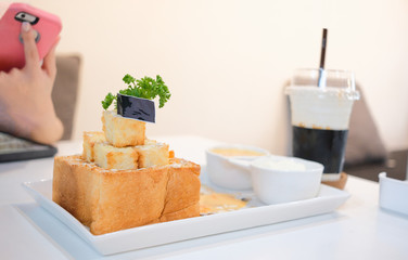 Girl take honey toast picture with salted egg sauce and ice-cream before eat. Set of dessert foods and drink at the cafe