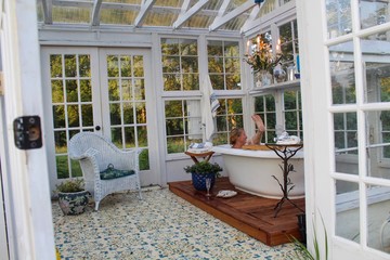 Happy and relaxed mature woman enjoying her beautiful greenhouse with a soaking tub 
