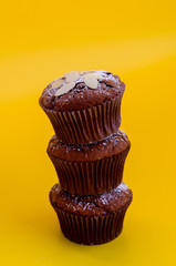 Three delicious chocolate muffins arranged on each other isolated on yellow back