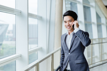 businessman using a cell phone, smiling. Taken in front of a modern office
