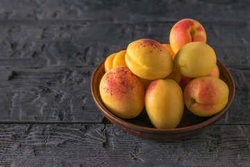 Bowl with ripe apricots on a black rustic wooden table.